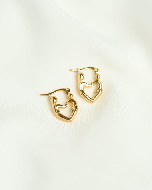 A pair of gold-toned hoop earrings with an open heart design mother & child, displayed on a soft, draped white fabric background.
